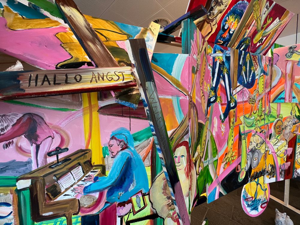 Close-up van het kunstwerk 'Hallo Angst', waarop schilderingen van mensen te zien zijn, met figuren in verschillende kleuren.
